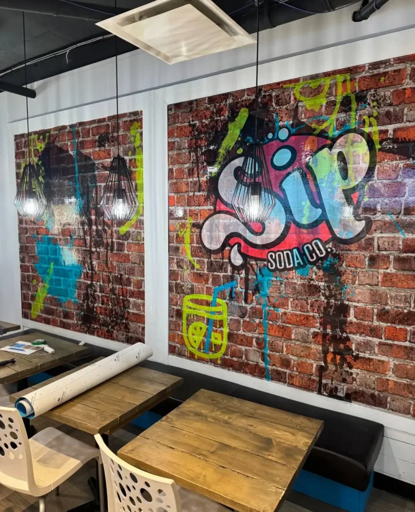 Interior of Sip Soda shop with tables, chairs, and graffitied brick wallpaper